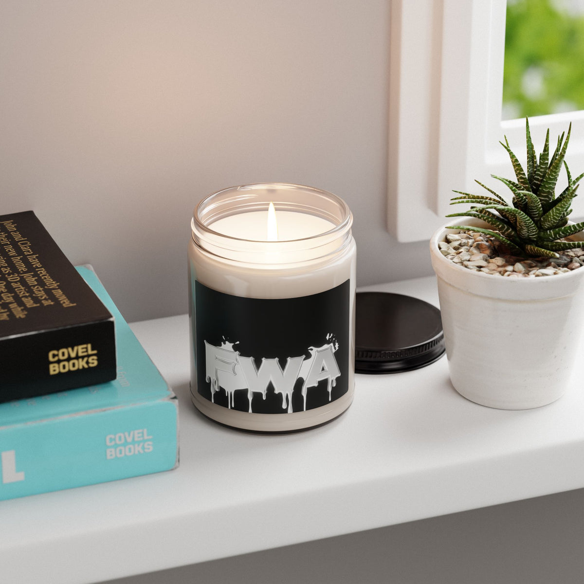 9oz Scented Soy Candle in a glass jar with a black label featuring a white 'FWA' drip logo, burning on a shelf.